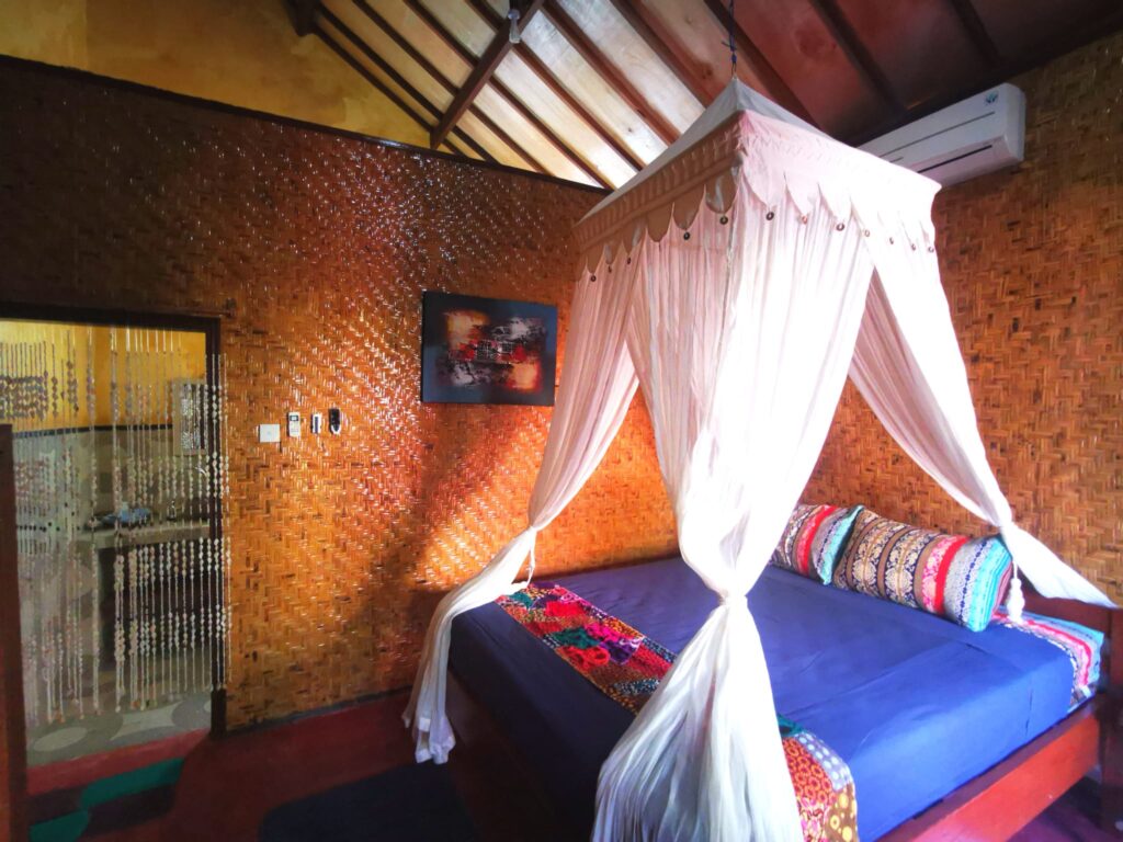 Air-conditioned bungalow room with a four-poster bed and mosquito net at Kampung Meno Bungalows